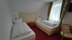 Hotellihuone, jossa on kaksi erillistä sänkyä, puinen yöpöytä, tuoli ja seinälle asennettu televisio.