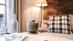 A neatly arranged table with a bottle, glasses, and a candle on a coaster. A lamp and a checkered pillow are on a wooden headboard. - Steinberghaus Top 3 (Rain)