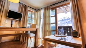 A cozy room with a wooden table, chairs, a TV, and a window with a mountain view. - Steinberghaus Top 3 (Rain)