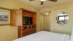 Une chambre avec un grand lit, une commode en bois, un ventilateur de plafond et un miroir au mur.