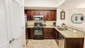 Una cocina con armarios de madera oscura, un microondas de acero inoxidable, una estufa a gas y un lavavajillas.