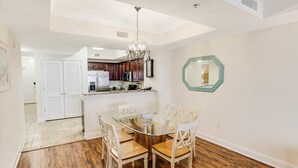 Un comedor con una mesa de vidrio y sillas de madera, una cocina al fondo y un espejo hexagonal en la pared.