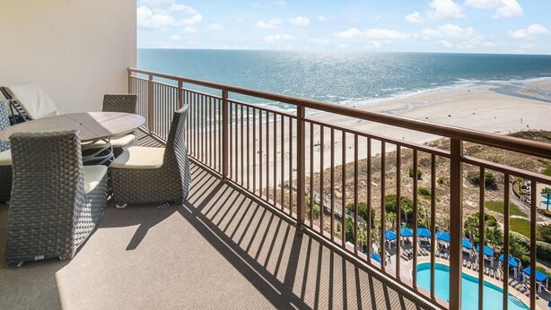 Ein Balkon mit Korbmöbeln, Blick auf den Strand und ein Poolbereich.
