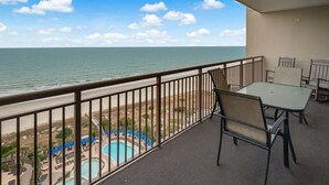 A balcony with a view of the ocean, a pool, and a table with chairs. - Sip Coffee with a View: 3 Bedroom Oceanfront Condo (North Myrtle Beach)