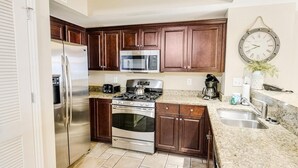 A kitchen with dark wooden cabinets, stainless steel appliances, a granite countertop, and a wall-mounted clock. - Sip Coffee with a View: 3 Bedroom Oceanfront Condo (North Myrtle Beach)