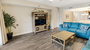 A living room with a blue sofa, a wooden coffee table, and a cabinet with 'BEACH' signage. - Sip Coffee with a View: 3 Bedroom Oceanfront Condo (North Myrtle Beach)