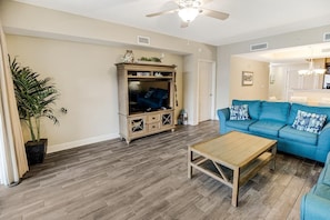A living room with a blue sofa, a wooden coffee table, and a cabinet with 'BEACH' signage. - Sip Coffee with a View: 3 Bedroom Oceanfront Condo (North Myrtle Beach)