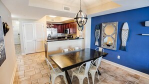 A kitchen with a dining area, white chairs, a black table, and a blue accent wall. - Serenity by the Sea: 3 Bedroom Beachfront Condo (North Myrtle Beach)