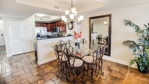 A dining area with a glass table and metal chairs, a chandelier, and a potted plant. - Coastal Retreat 3 Bedroom Oceanfront 4th Floor (North Myrtle Beach)