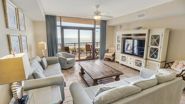 A spacious living room with a large sofa, a coffee table, and a television. There is a balcony with a view of the ocean. - Relax in Style 3 Bdrm Condo with King and Queen (North Myrtle Beach)