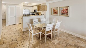 A modern kitchen with white cabinets, a stainless steel refrigerator, and a hanging light fixture. - Relax in Style 3 Bdrm Condo with King and Queen (North Myrtle Beach)