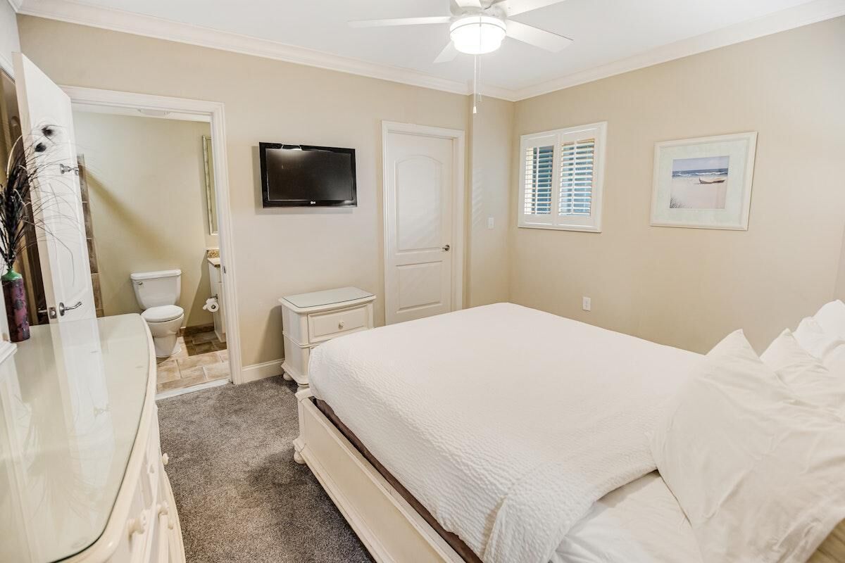 A bedroom with a bed, a television, a door, a window, and a bathroom visible through an open door.