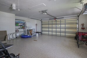 Eine Garage mit Betonboden, einer Metalttür und verschiedenen Gegenständen wie einem Stuhl, einem Eimer und einem Wagen.