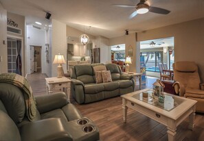 A spacious living room with a green leather sofa, a glass coffee table, and a ceiling fan. - FABULOUS NEW BONITA POOL HOUSE! PET FRIENDLY! MINUTES TO BEACHES! (Bonita Springs)