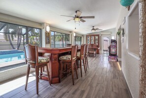 A dining area with a pool view, wooden chairs, a bar, and ceiling fans. - FABULOUS NEW BONITA POOL HOUSE! PET FRIENDLY! MINUTES TO BEACHES! (Bonita Springs)