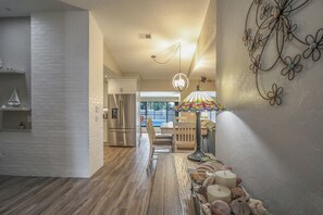 A hallway with a wooden floor, a dining area with a table set for two, and a kitchen with a stainless steel refrigerator. - FABULOUS NEW BONITA POOL HOUSE! PET FRIENDLY! MINUTES TO BEACHES! (Bonita Springs)