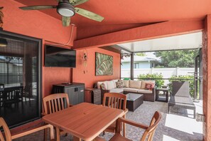 Un espacio de patio al aire libre con mesa y sillas de madera, un sofá y una televisión montada en la pared.