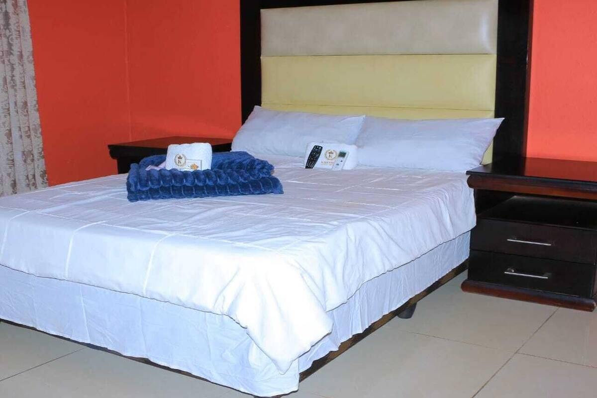 A neatly made bed with white bedding, a blue decorative item, and a bedside table with a remote control.