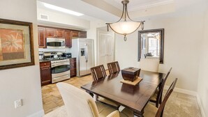 A dining area with a wooden table and chairs, a chandelier, and a kitchen in the background. - 2nd Flr Oasis: Oceanfront Bliss with King Bed (North Myrtle Beach)