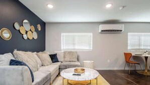 A modern living room with a sectional sofa, a round coffee table, and decorative wall art. - Walk to Oaklawn Casino! Luxe Studio w/King Bed (Hot Springs)