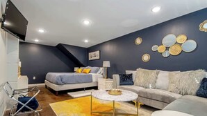A modern living room with a bed, sofa, and coffee table, featuring a dark wall with decorative mirrors and a mounted TV. - Walk to Oaklawn Casino! Luxe Studio w/King Bed (Hot Springs)