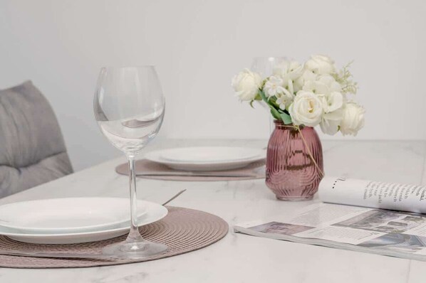 Una mesa de comedor con una copa de vino, platos, un florero con flores blancas y un periódico.