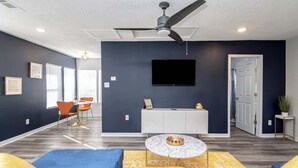 A living room with a ceiling fan, a flat-screen TV, a round coffee table, and a sofa with cushions. - Luxury Studio, 3-Min Walk to Oaklawn Casino (Hot Springs)