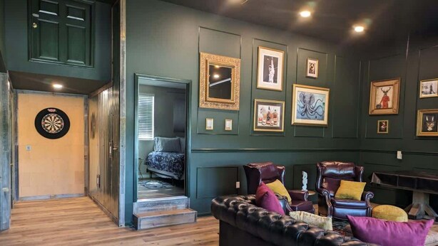 A room with a leather sofa, framed artwork on the wall, and a dartboard. - Lakeside Chalet w/Game Room & Private Boat Slip (Garland County)