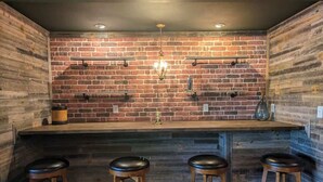 A bar area with a brick wall, wooden bar counter, and three stools. - Lakeside Chalet w/Game Room & Private Boat Slip (Garland County)