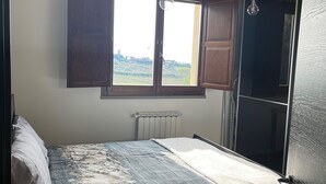 A bedroom with a bed, a radiator, a window with curtains, and a view of the outdoors. - Modern Countryside Condo with Views (San Quirico In Collina)