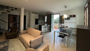 A modern living space with a sofa, dining table, and kitchen area. - Modern Countryside Condo with Views (San Quirico In Collina)