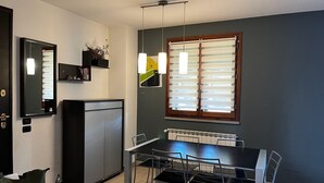 A dining area with a table and chairs, a refrigerator, a mirror, and a window with blinds. - Modern Countryside Condo with Views (San Quirico In Collina)