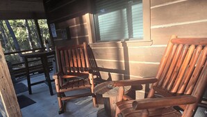 En rustik veranda av trä med två trästolar och ett bord.