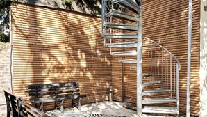 A wooden exterior wall with a metal spiral staircase, a bench, and a zebra-patterned rug.
