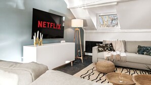 A modern living room with a flat-screen TV mounted on a wall, a white cabinet, a grey sofa, and a patterned rug.