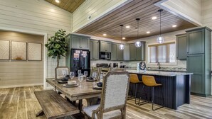 Een moderne keuken met houten vloeren, een centraal eiland met barkrukken en een eethoek met een houten tafel en stoelen.