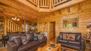 A wooden cabin interior with two leather sofas, a dining table, and a staircase.