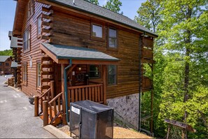 Une cabane en rondins dotée d’une véranda, d’un petit espace extérieur aménagé pour s’asseoir et de fondations en pierre.