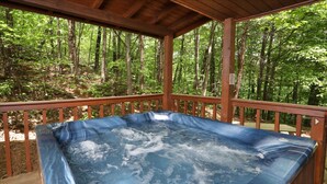 Ein Whirlpool auf einer Holzterrasse, umgeben von einem Wald.