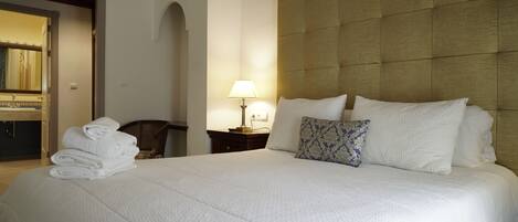 Una cama bien hecha con sábanas blancas, cabecera y lámpara de noche.