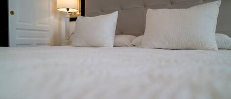 A neatly made bed with white linens and pillows, a tufted headboard, and a bedside lamp.