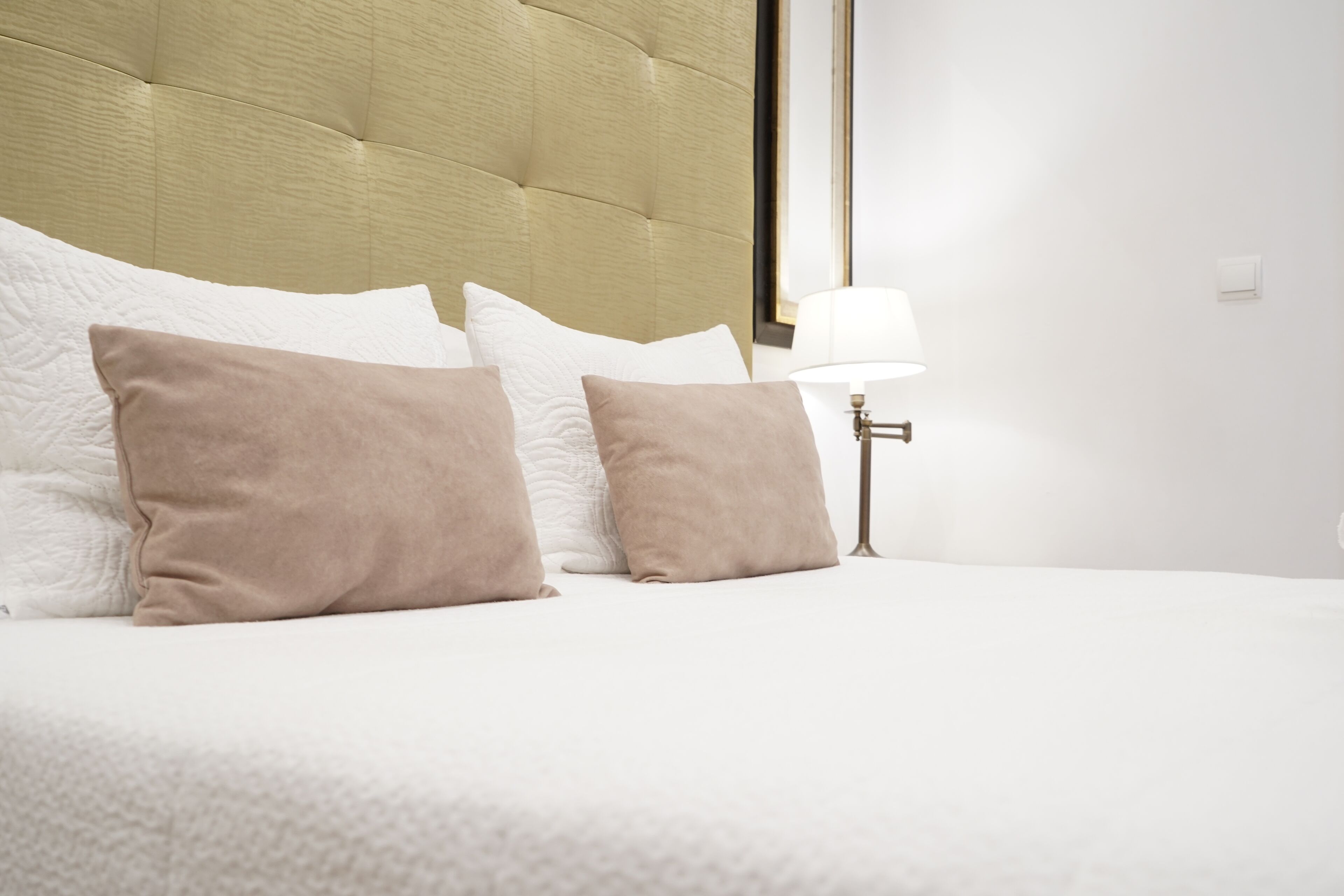 Una cama bien hecha con almohadas blancas y beige, un cabecero y una lámpara de noche.