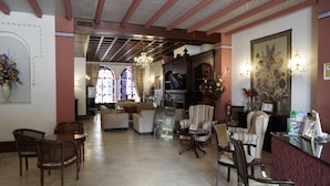 A spacious lobby with a high ceiling, a reception desk, comfortable seating, and a large window with stained glass. - Palacete Real (Almonte)