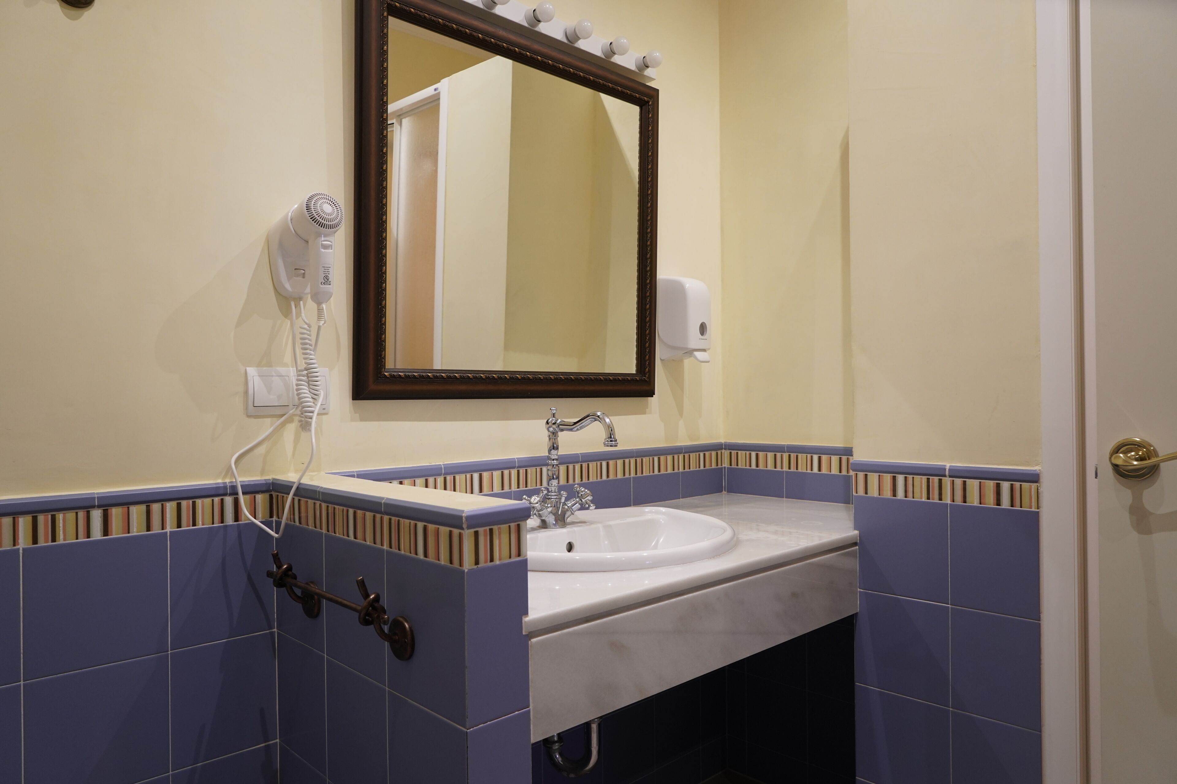 A bathroom with a sink, mirror, hairdryer, and towel rack.