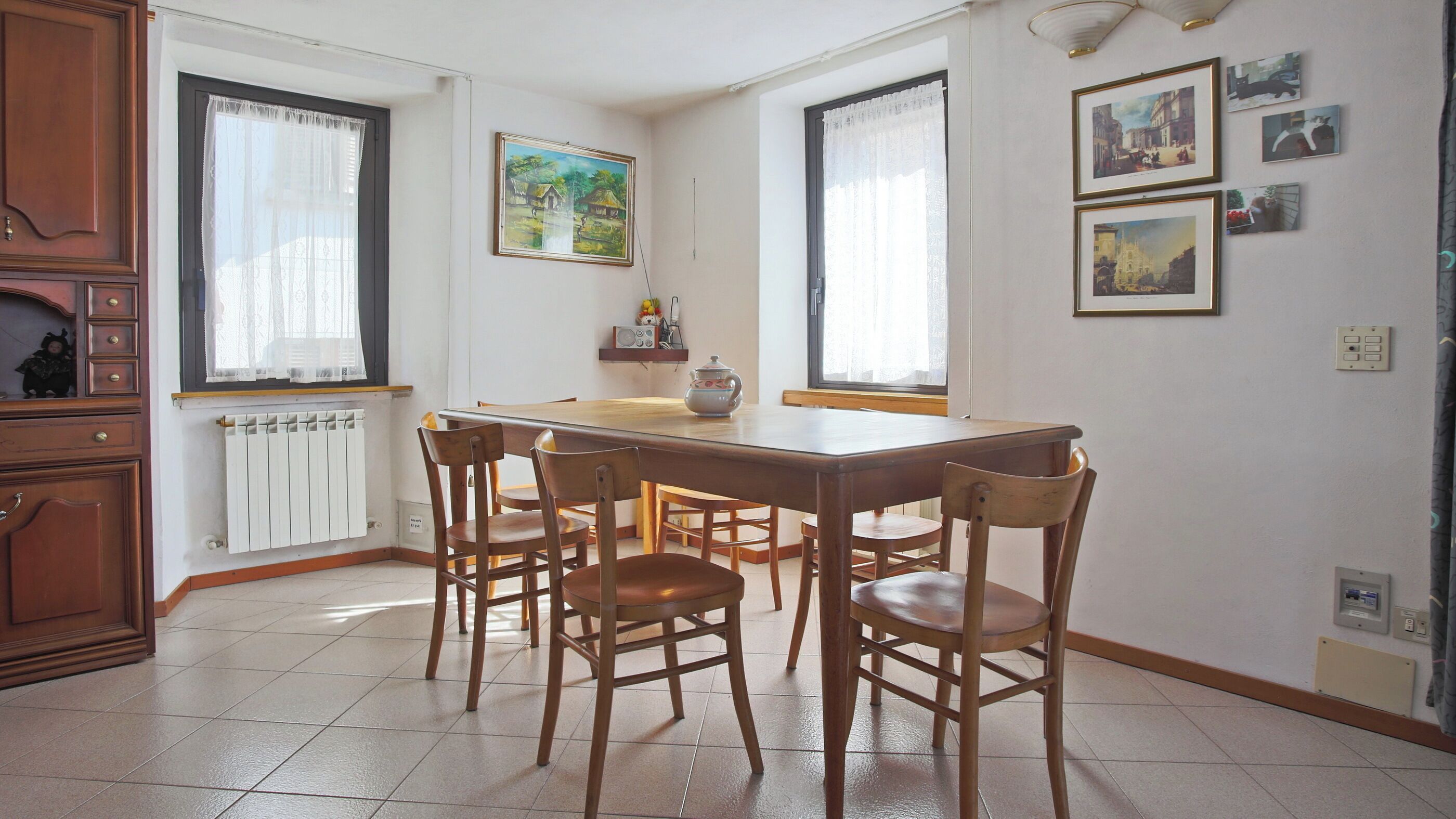 A dining area with a wooden table and chairs, a radiator, and a window with curtains.