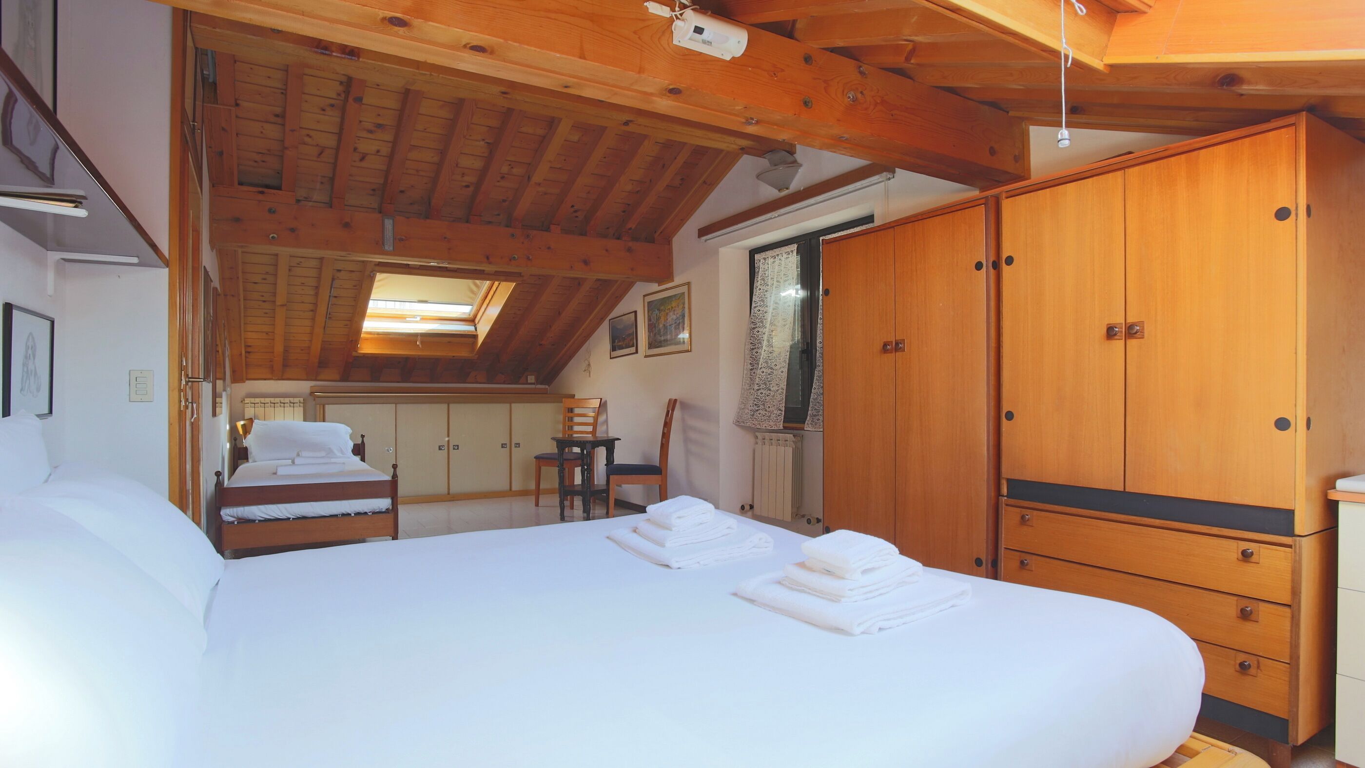 A bedroom with a large bed, wooden wardrobe, and a skylight.