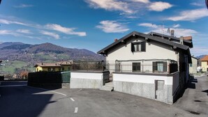Uma casa de dois andares com fachada de pedra, uma pequena varanda e vista para as montanhas ao fundo.