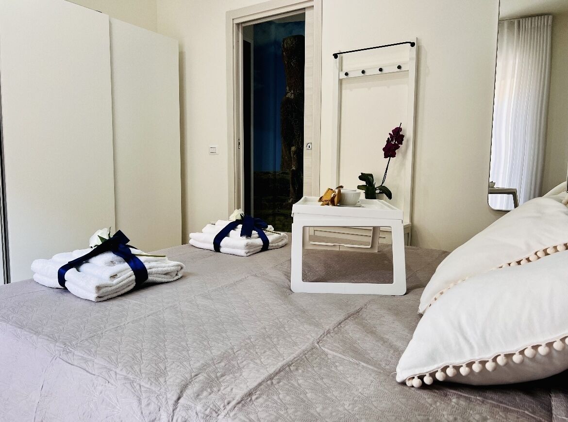 Habitación de hotel con cama, mesita de noche con espejo, una planta pequeña y toallas sobre la cama.