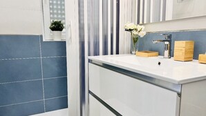Une salle de bain avec un lavabo blanc, des carreaux bleus, un miroir à rayures et une petite plante en pot.