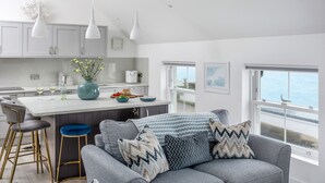 A modern kitchen with white cabinets, a central island, and pendant lighting. - Loe Cottage (Helston)